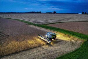 Colheitadeira iluminada opera em campo agrícola ao entardecer. A imagem remete aos impactos ambientais do biodiesel, como alterações no uso da terra.